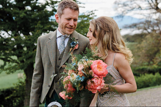 bride carries a colourful bouquet of flowers next to groom