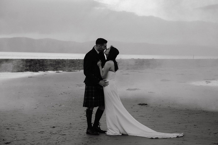 black and white photograph of bride and groom standing on dougarie boathouse beach
