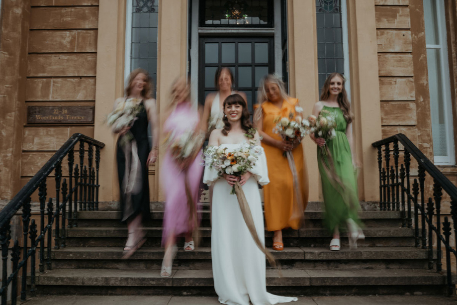 The bride posing on a set of stairs with bridesmaids behind her