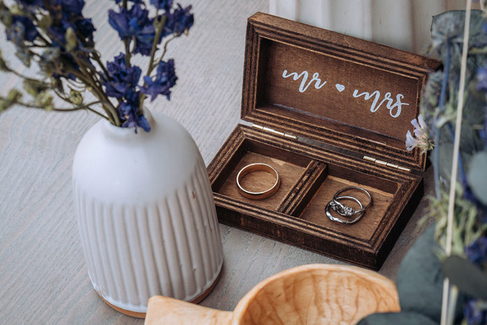 A wooden ring box with "Mr and Mrs" with wedding rings inside, with flowers in foreground