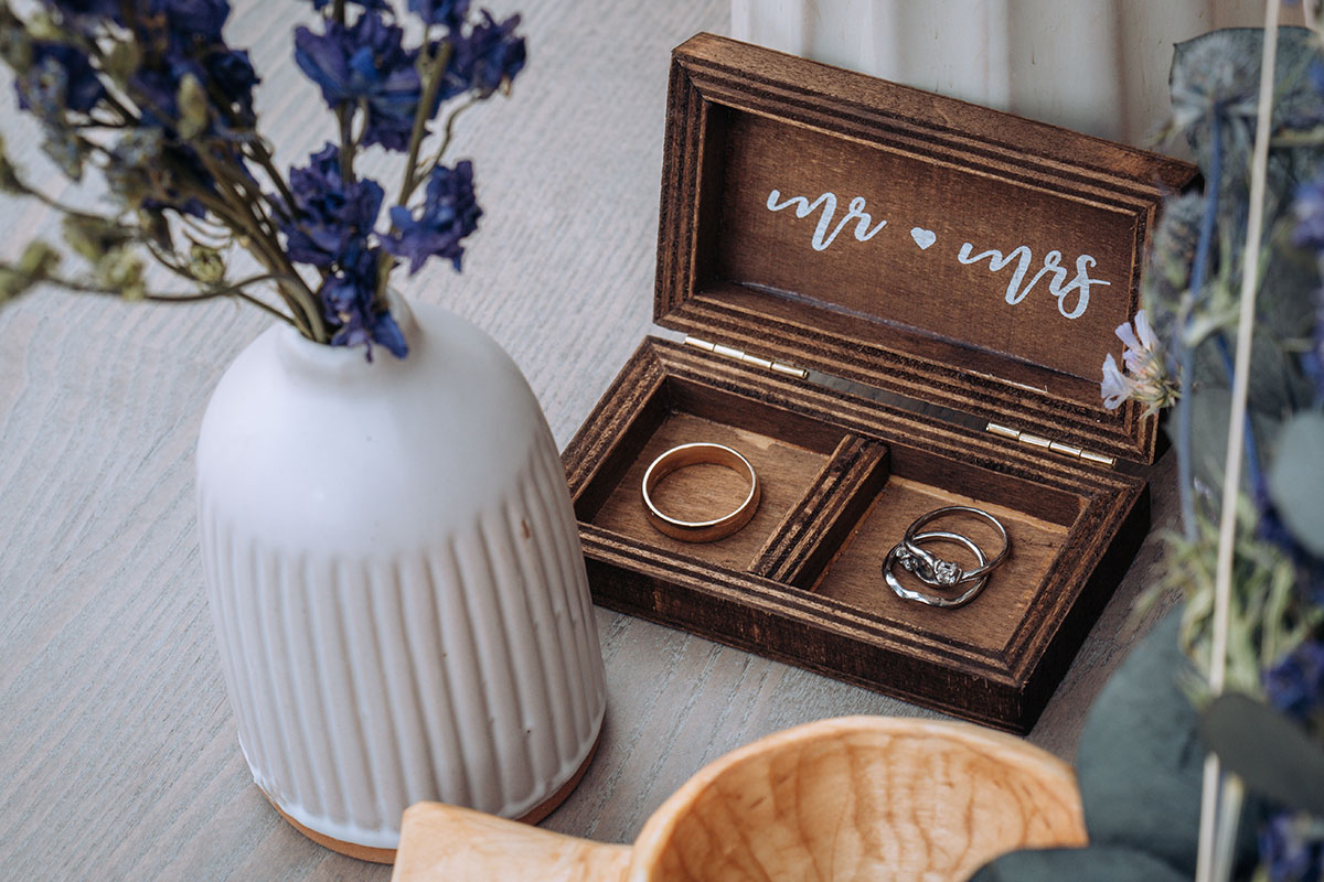 A wooden ring box with "Mr and Mrs" with wedding rings inside, with flowers in foreground