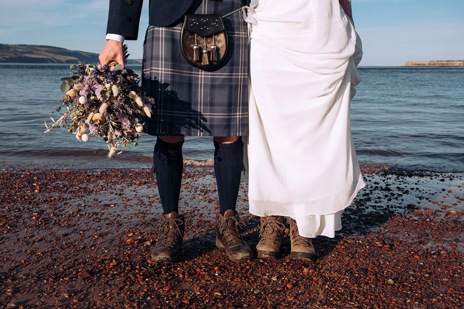 Bottom half of bride and groom wearing walking boots and standing on a beach