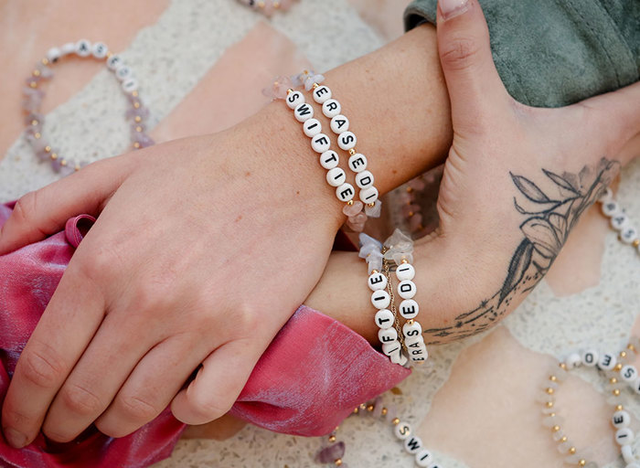 A close up of two wrists holding onto each other, both wearing two friendship bracelets with letter beads 