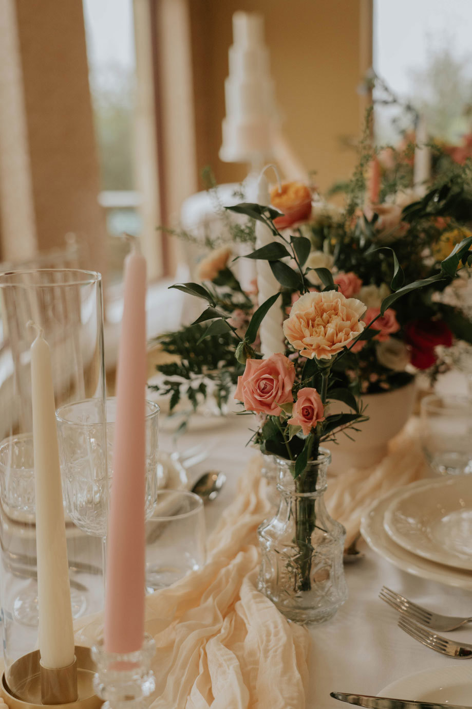 A table set with pink and orange flowers, pink and white candles, plates and cutlery 