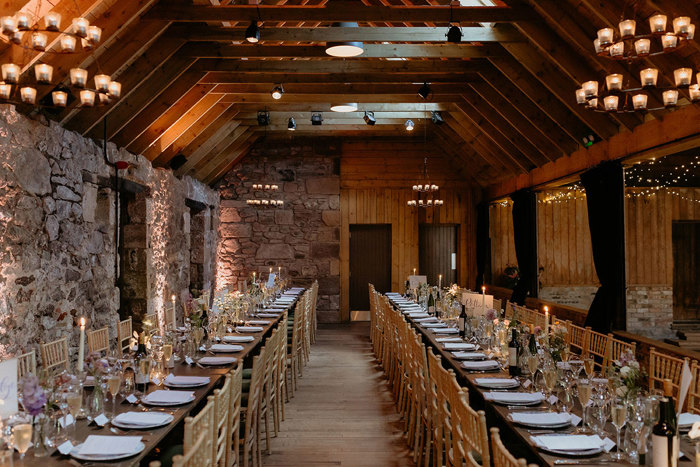 the Byre at Inchrya set up for a wedding dinner with long wooden tables and chiavari chairs