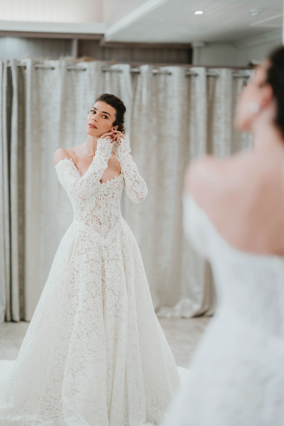 Bride trying on a long-sleeved lace wedding dress with a full skirt at Opus Couture.