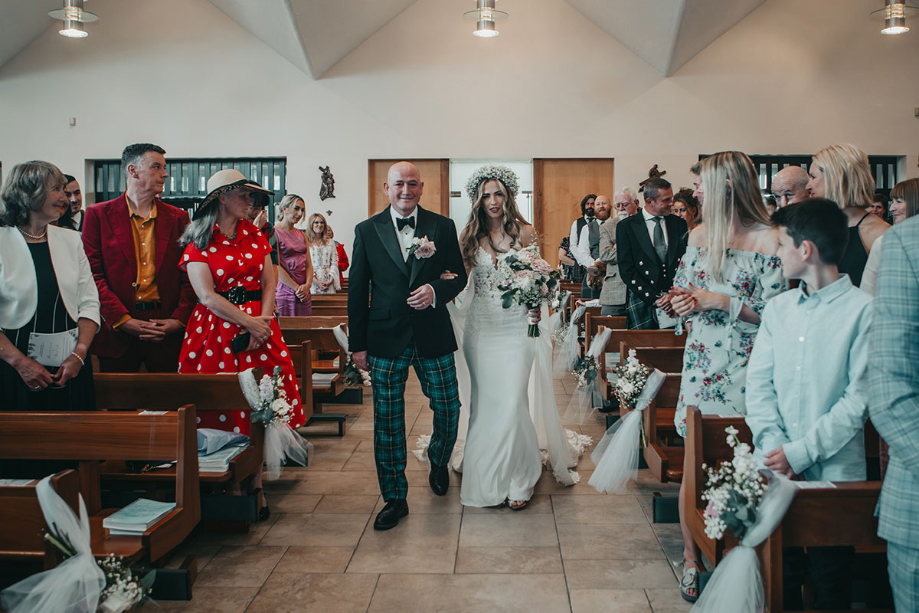 Bride is walked down the aisle by her dad while carrying a bouquet 