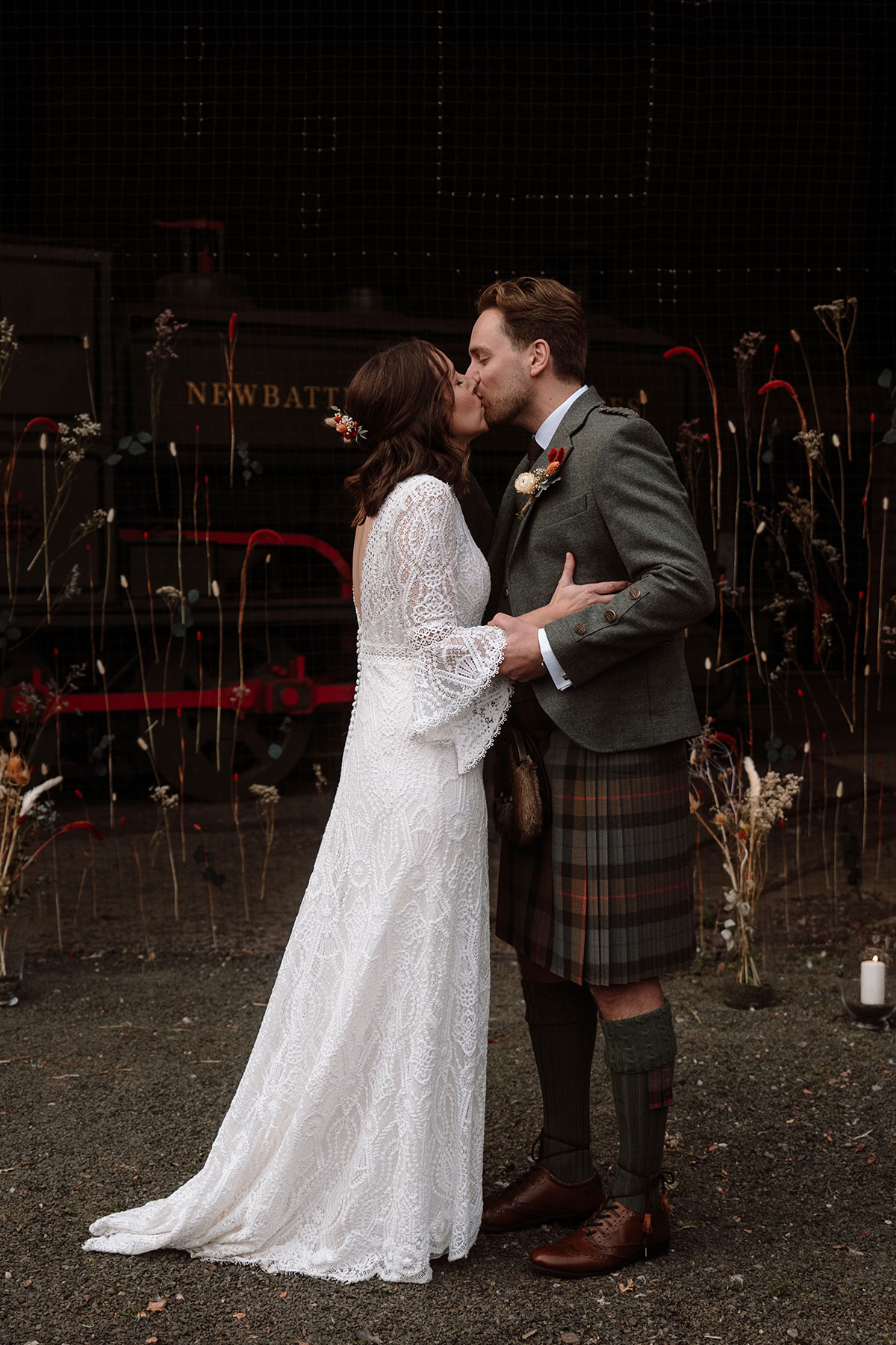 Bride and groom share a kiss following their wedding ceremony, standing in front of a floral installation at an industrial wedding venue