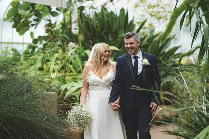 A bride and groom holding hands surrounded by plants in Glasgow Botanic Gardens Kibble Palace