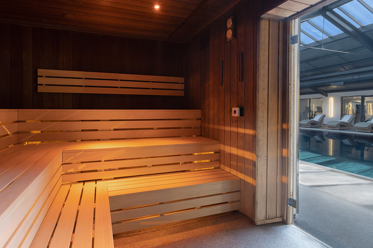 the lit up inside of a wooden benched sauna with a glass door looking out to a swimming pool