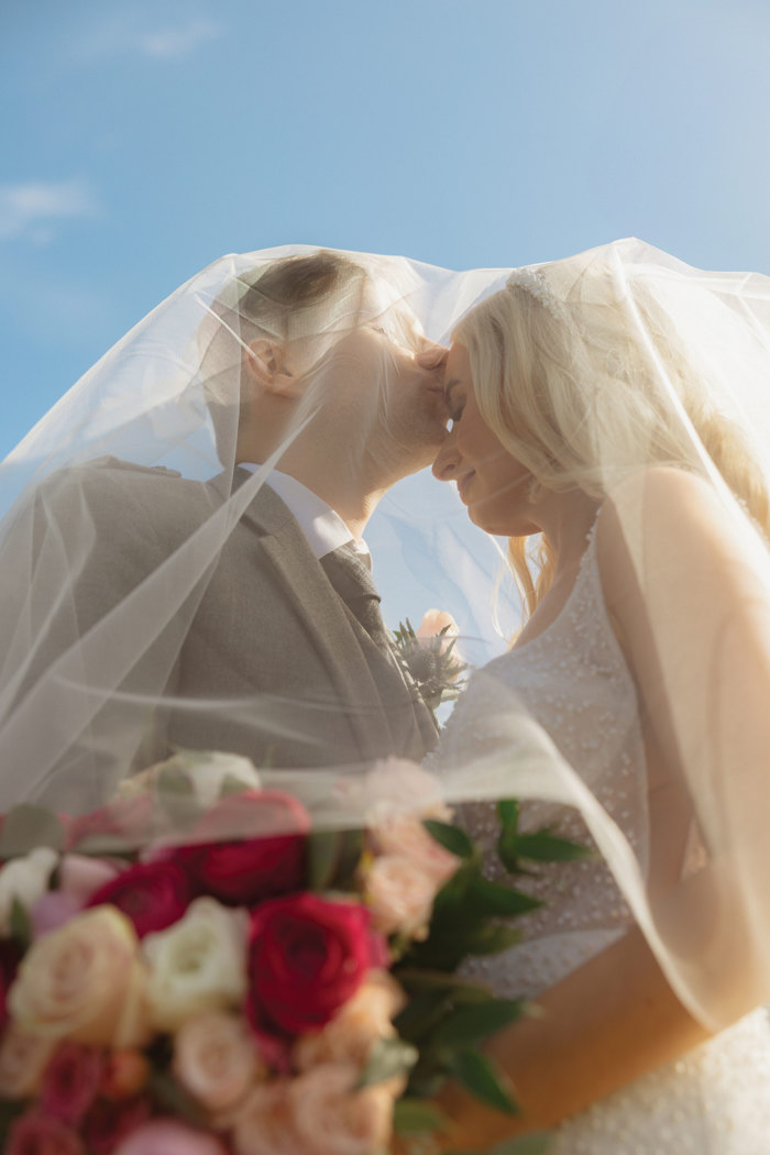 bride and groom under veil in the sunshine with roses in focus
