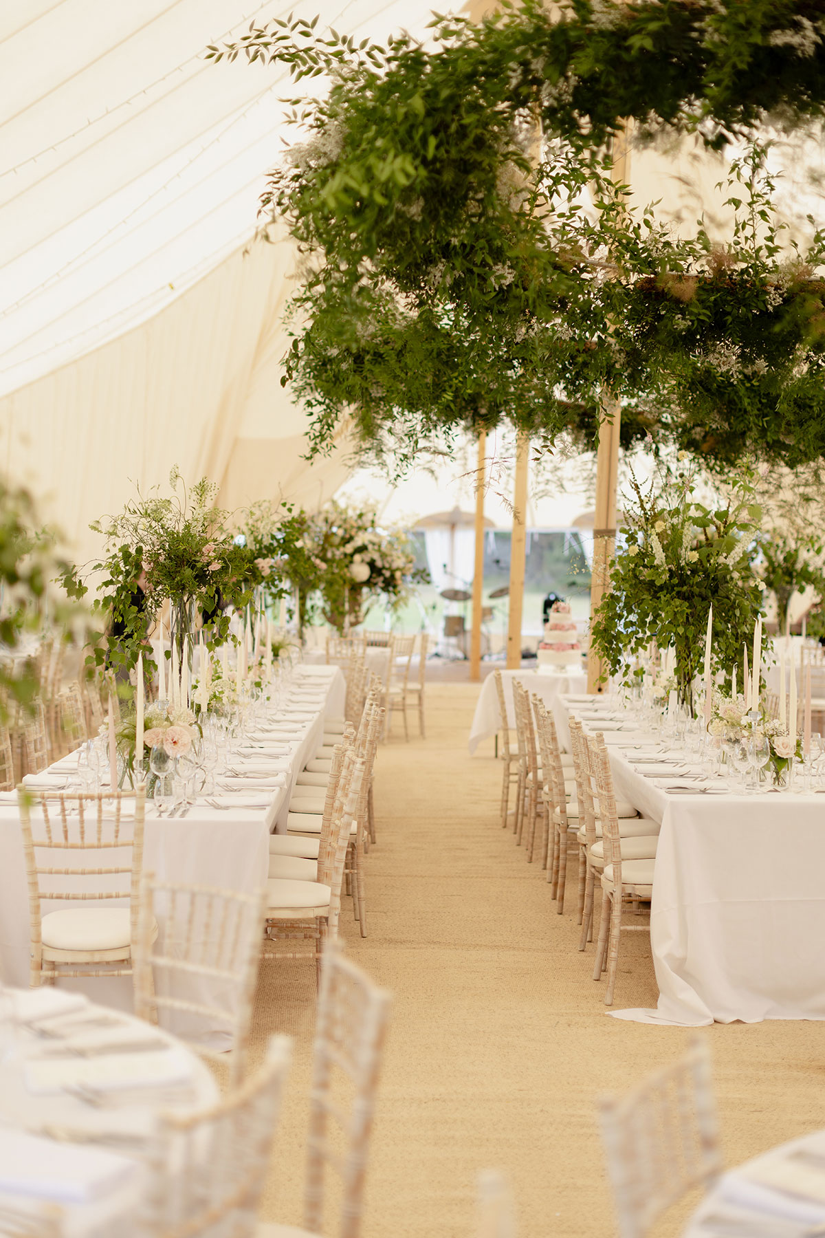 Wedding marquee featuring long banquet tables, soft neutral décor and overhead greenery installations creating a natural, modern look.