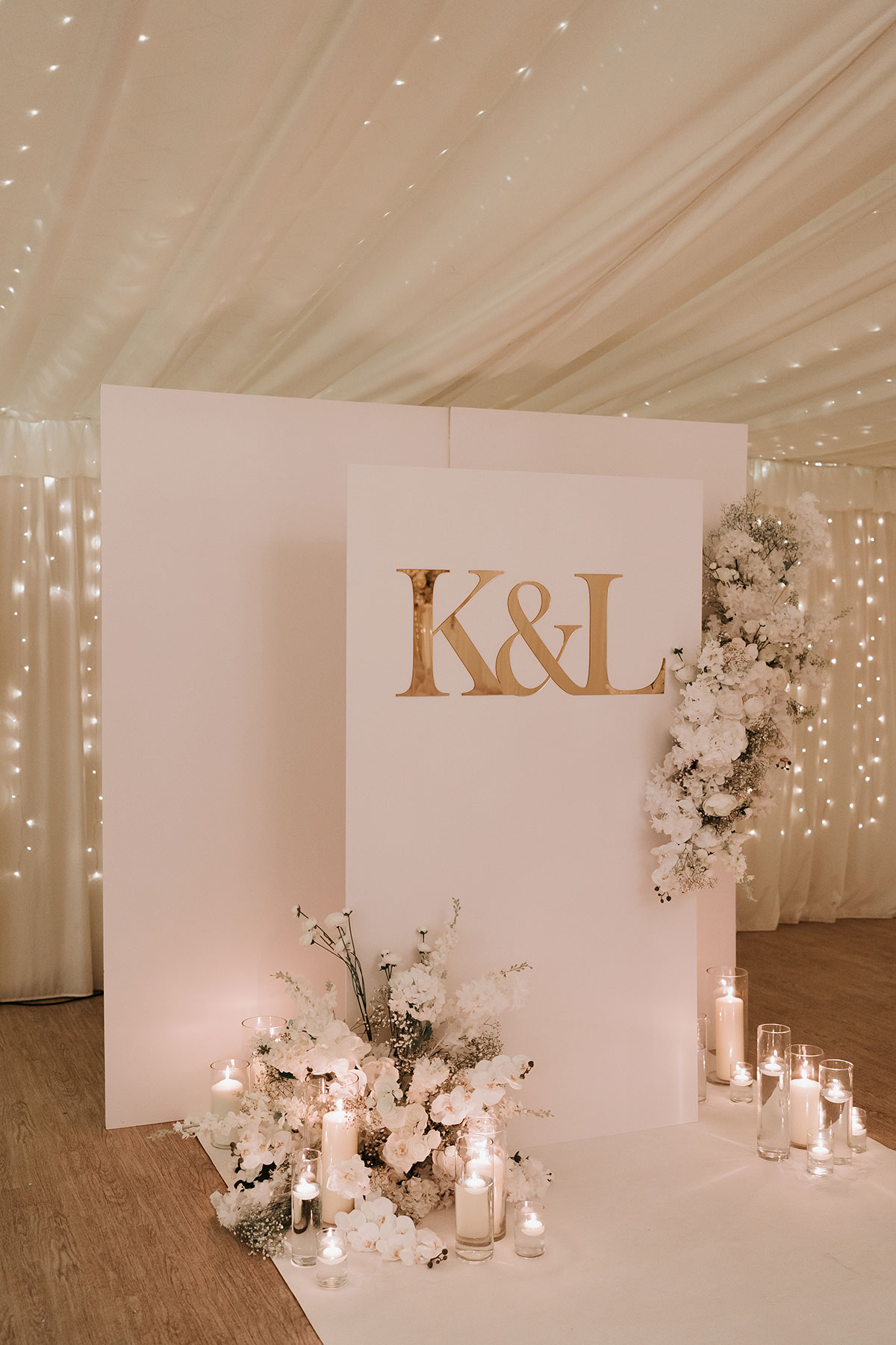 White ceremony backdrop with gold initials, floral arrangements and candles at Ingliston Country Club