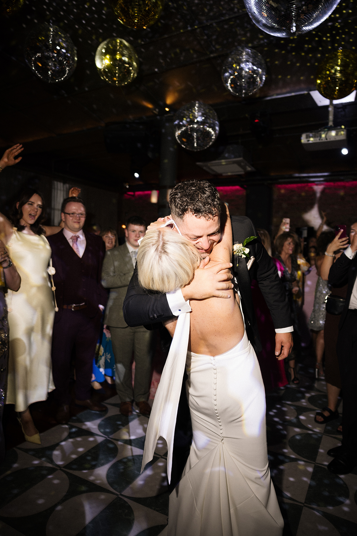 Bride and groom kissing on the dancefloor under disco balls at their evening reception