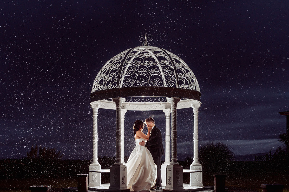 The Waterside Hotel’s outdoor wedding bandstand at night, with a bride and groom standing beneath the illuminated structure.