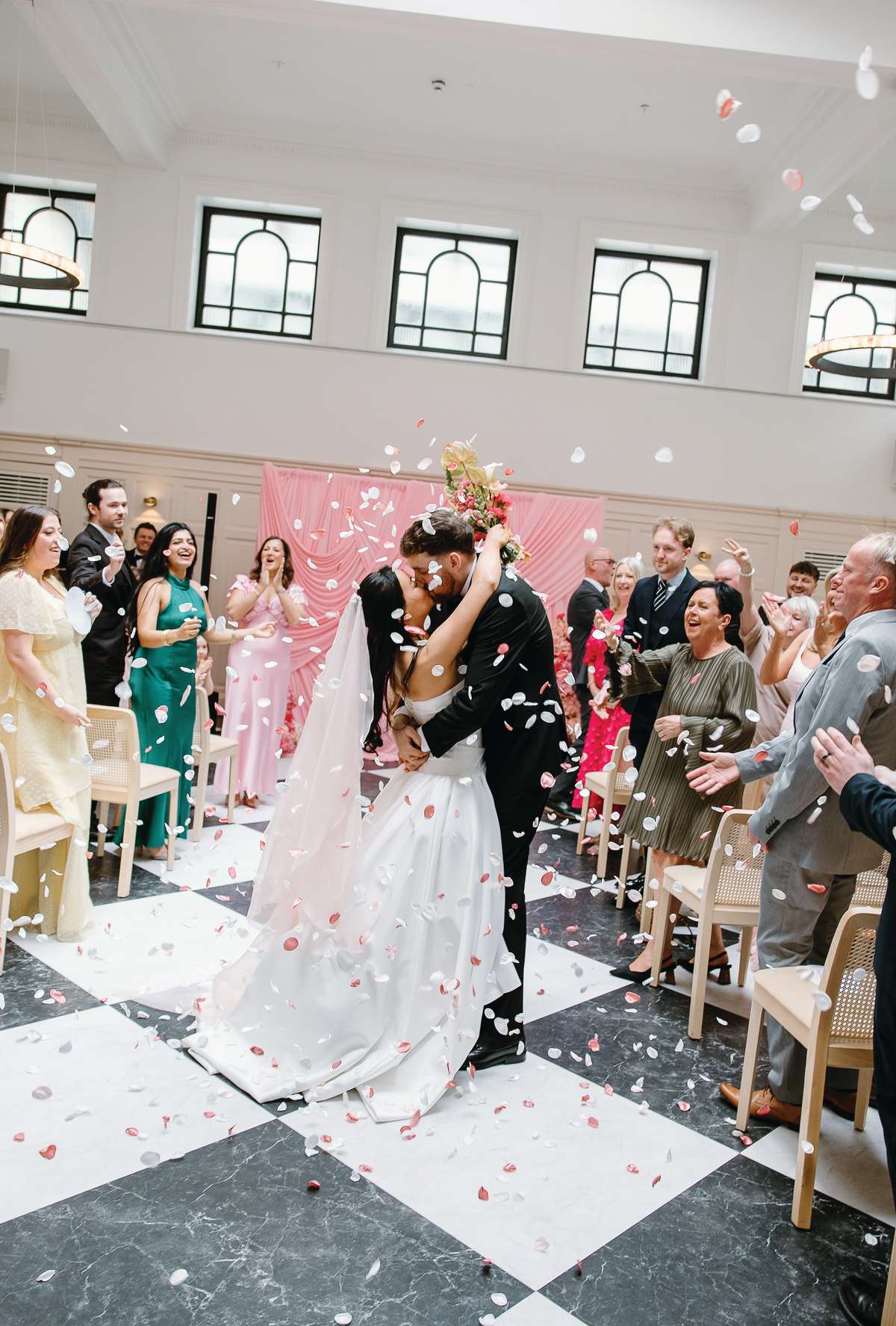 Bride and groom kiss beneath a shower of pink and white confetti following their wedding ceremony at The Collector’s Hall Glasgow.