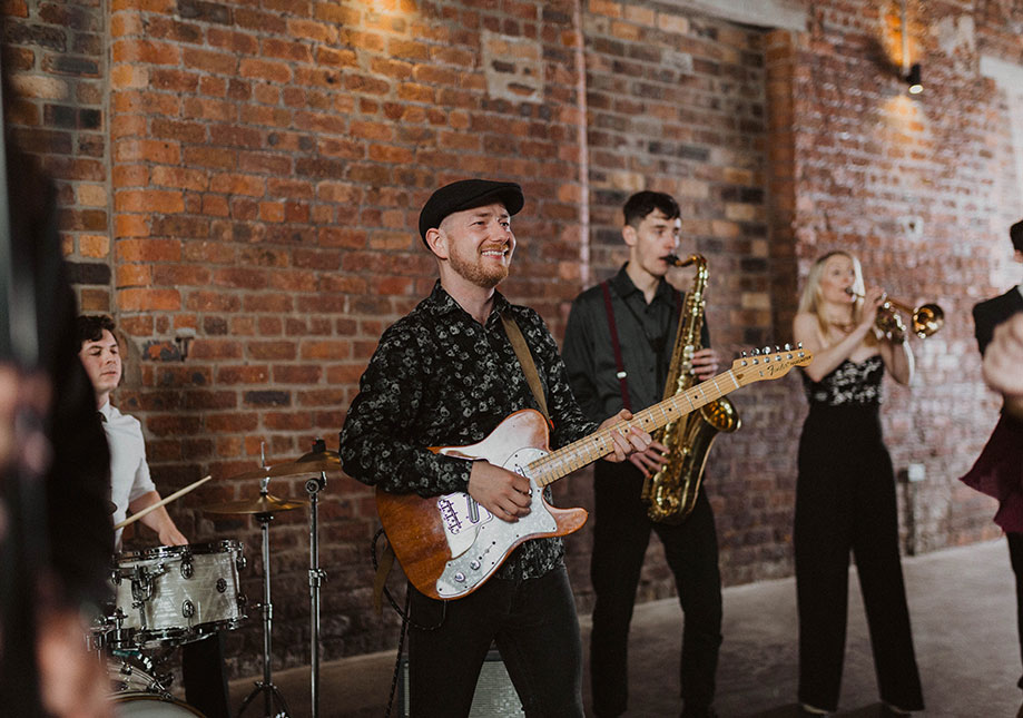 a group of people playing musical instruments standing against a red brick wall