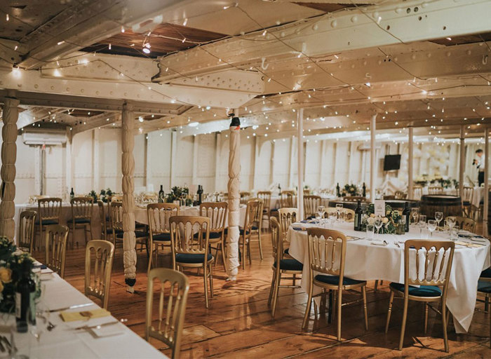 A room with round tables and wooden chairs and fairylights hanging from the ceiling 