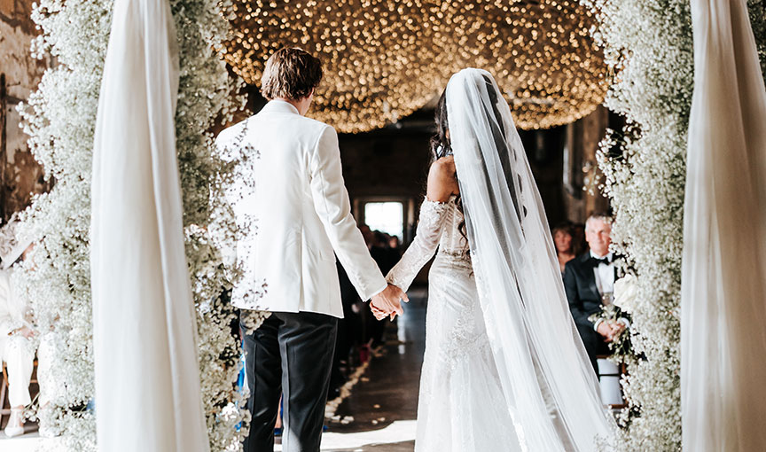 Couple entering at Falside Mill wedding ceremony hand in hand beneath an arch of baby’s breath and a ceiling of fairy lights.
