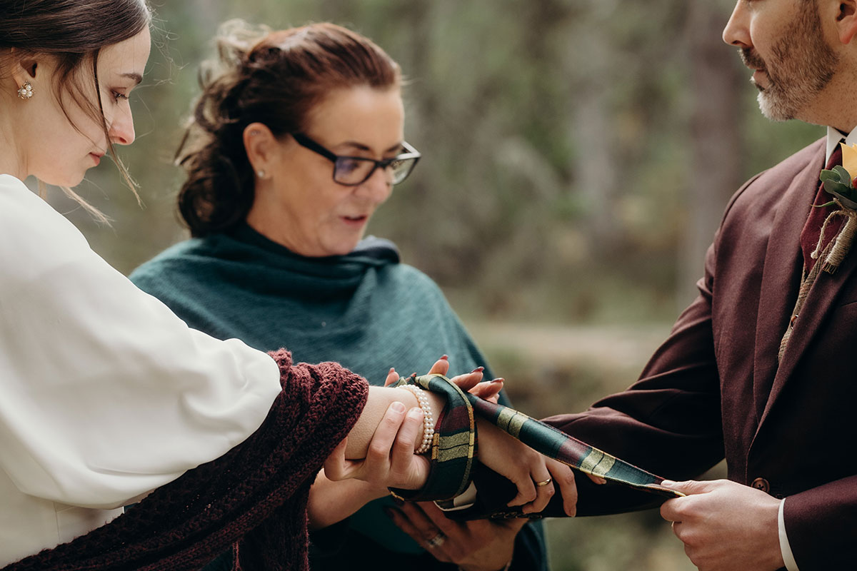 Outdoor wedding ceremony with tartan ribbon handfasting on River Quoich at Mar Lodge Estate