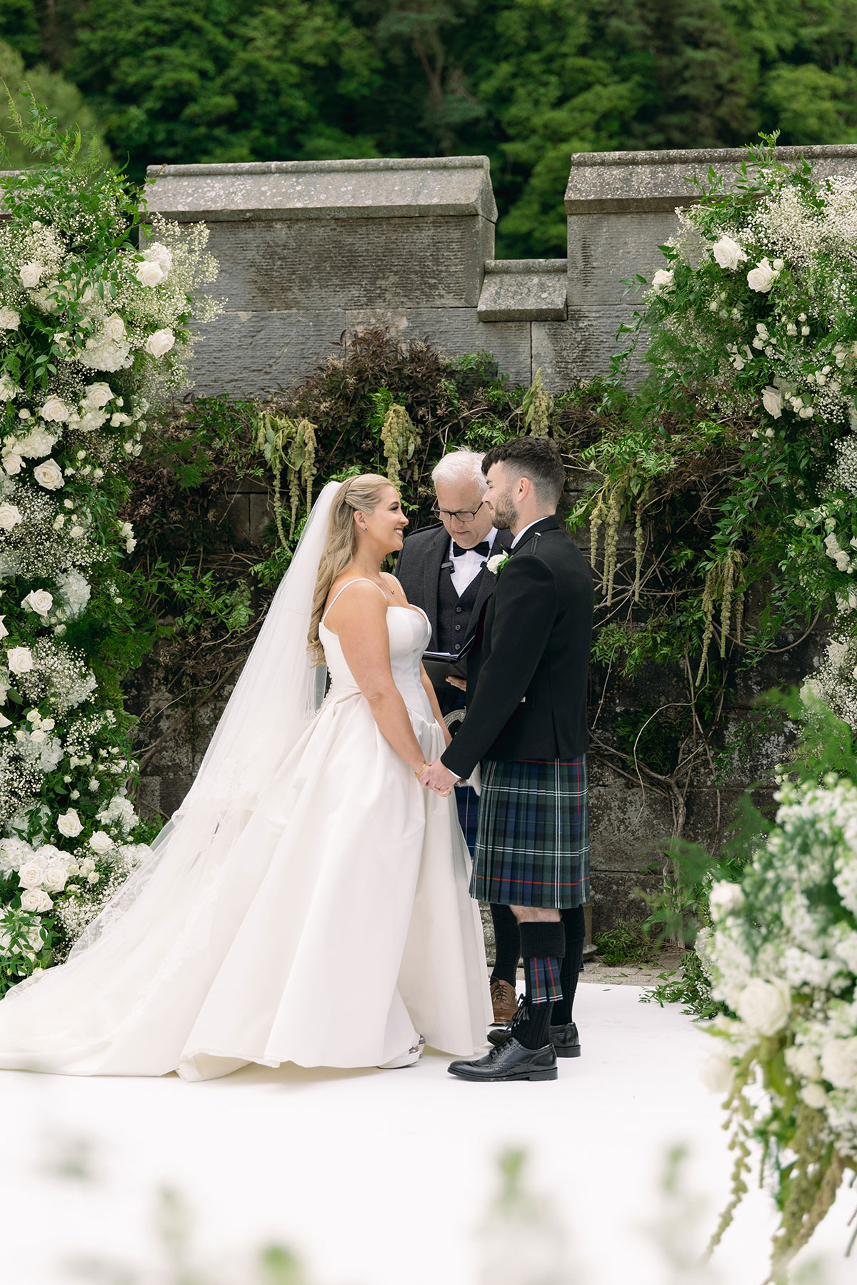 Elegant white rose and greenery floral arrangements frame Dundas Castle outdoor wedding ceremony.