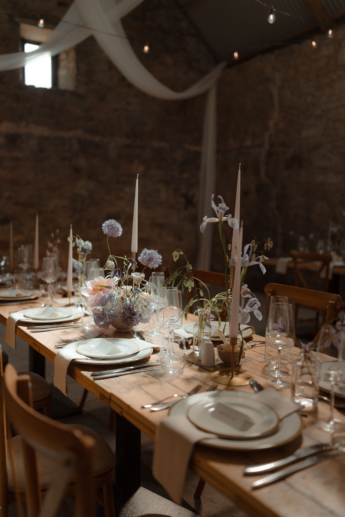 Candlelit wedding reception tables with soft draping and floral centrepieces inside converted barn near Falkirk