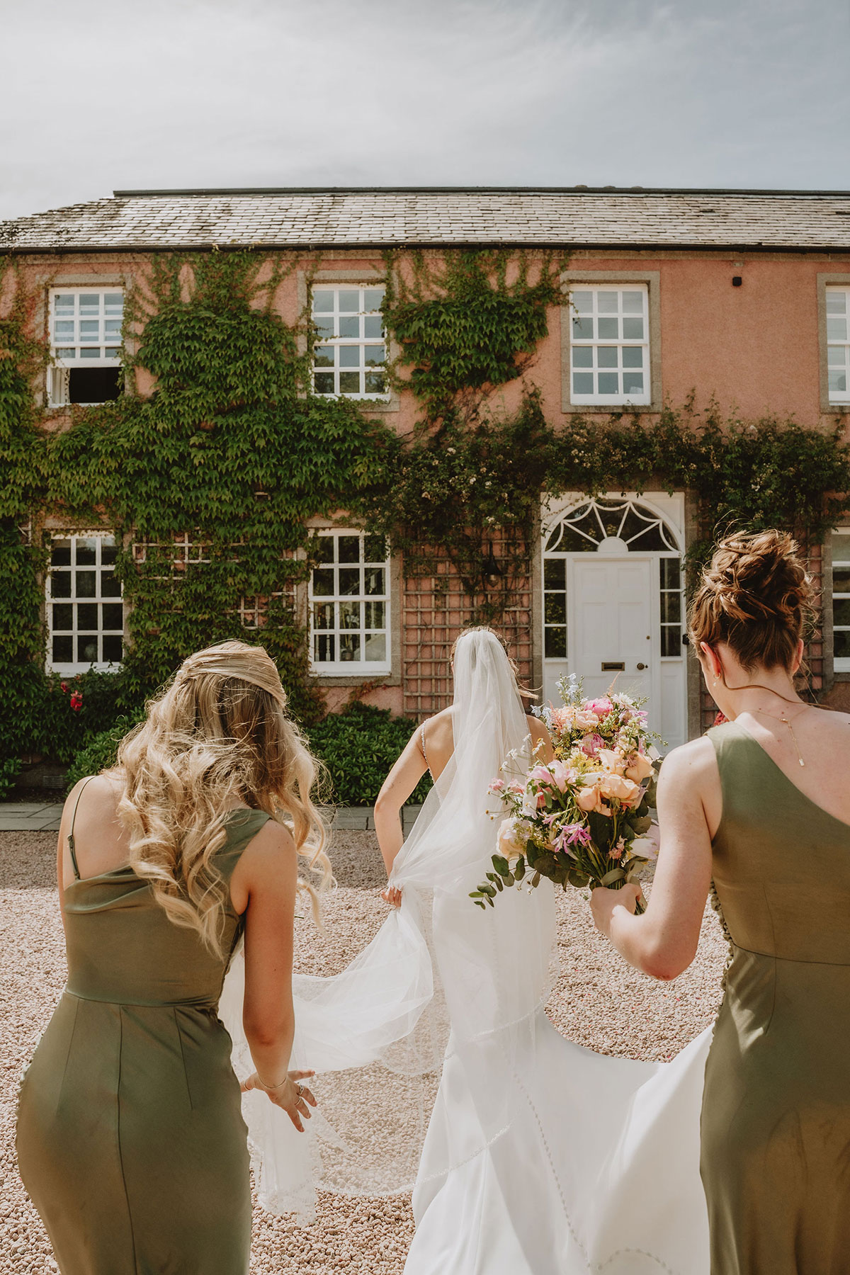 Bride walking with bridesmaids across the courtyard outside Ballogie House before the ceremony