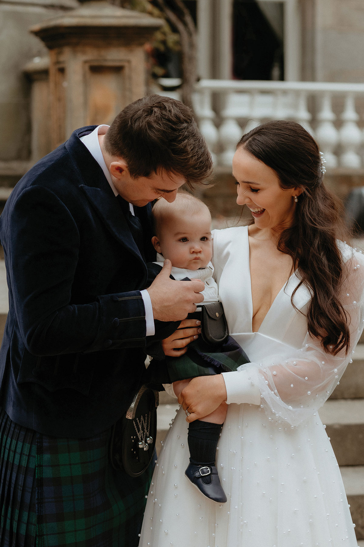 a bride and groom with a baby wearing a small kilt outfit
