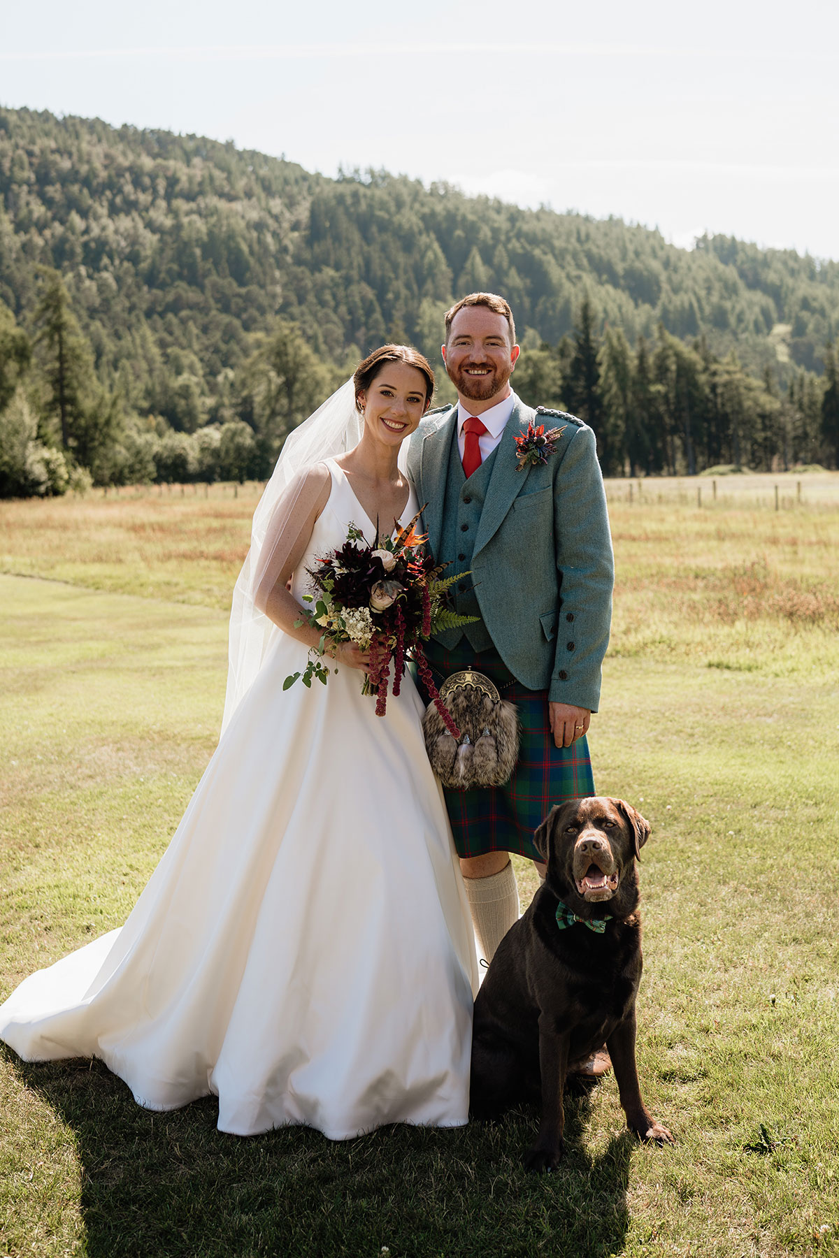 Bride and groom posing with their chocolate Labrador after their Scottish Highlands wedding at Mar Lodge Estate