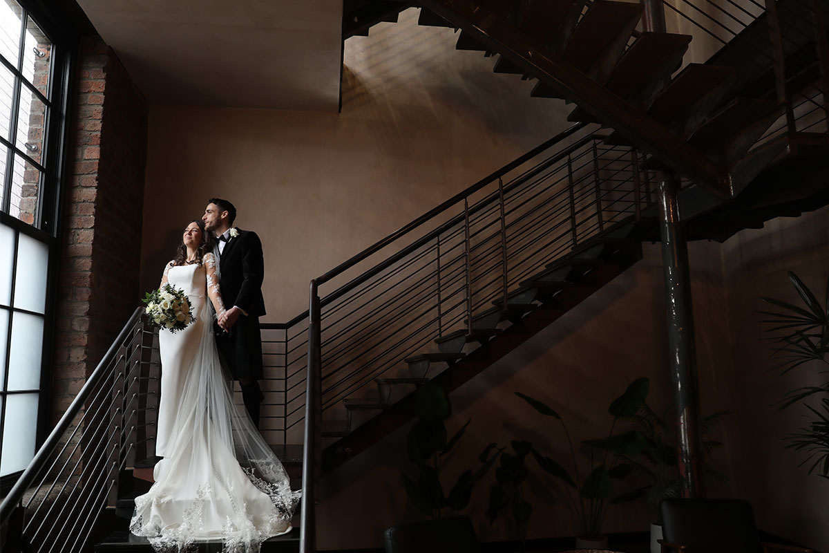 A bride and groom standing on a set of stairs looking out of a window