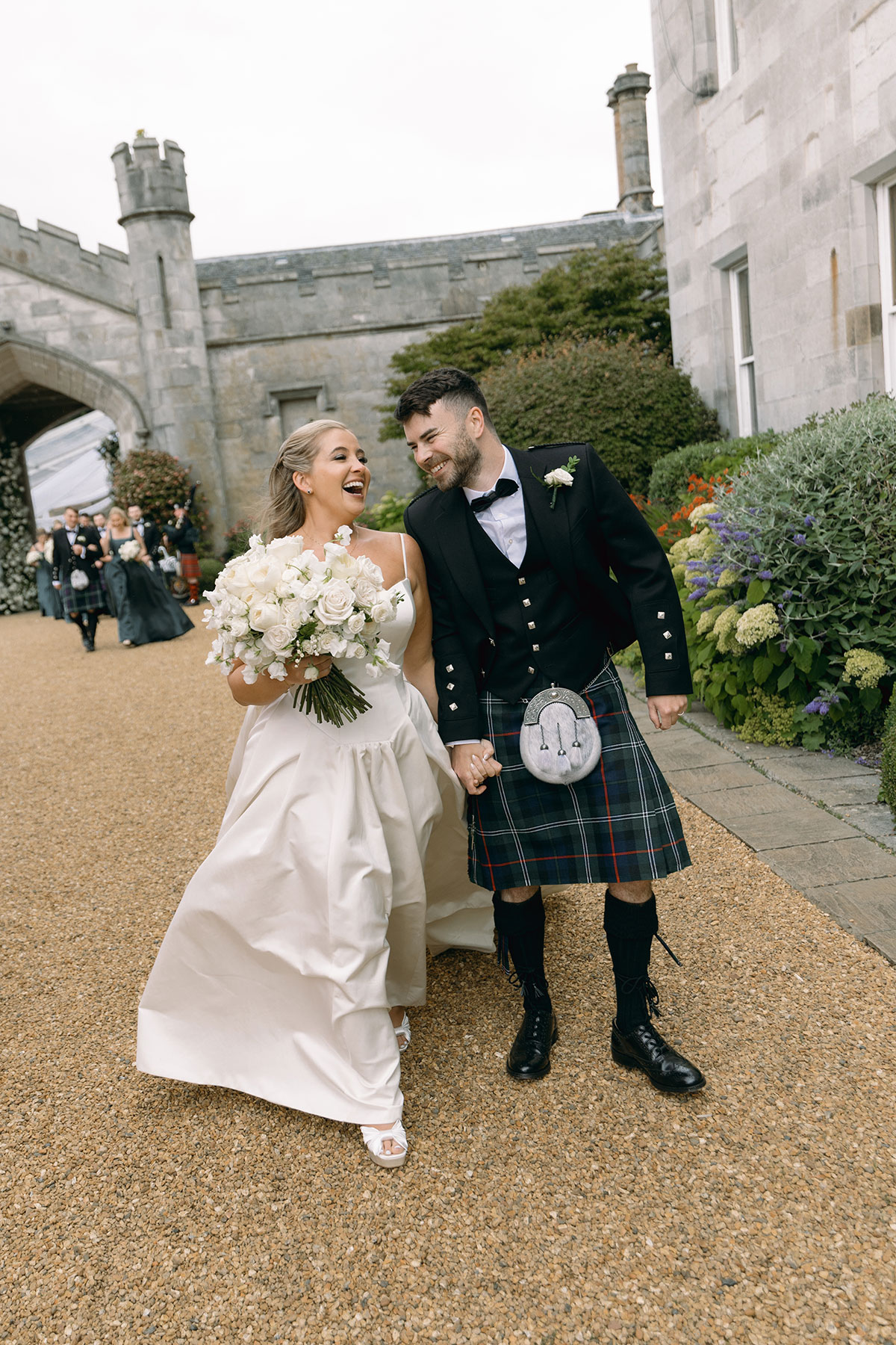 Bride and groom walk hand in hand outside Dundas Castle, laughing after their romantic Scottish wedding ceremony.