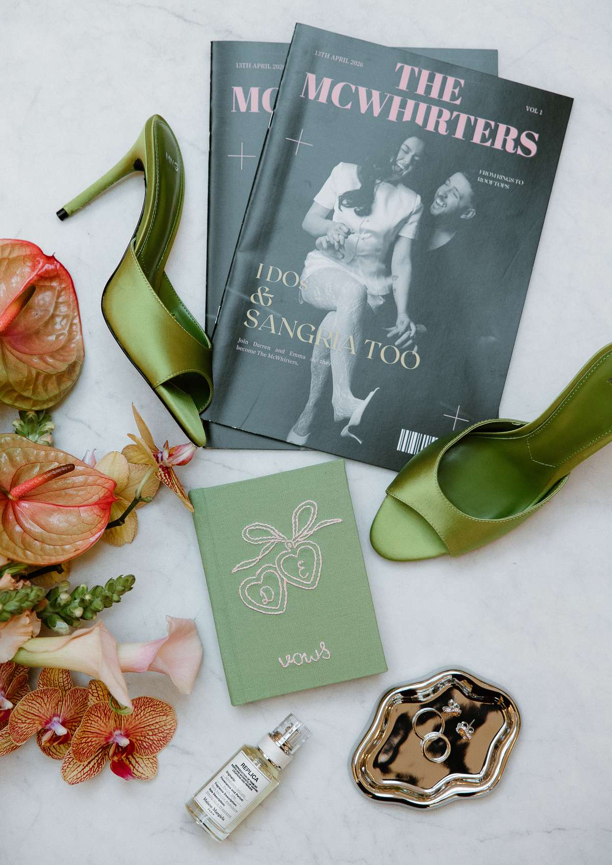 Personalised McWhirters wedding magazines, green bridal shoes, vow book, wedding rings and colourful flowers arranged for a stylish flat lay.