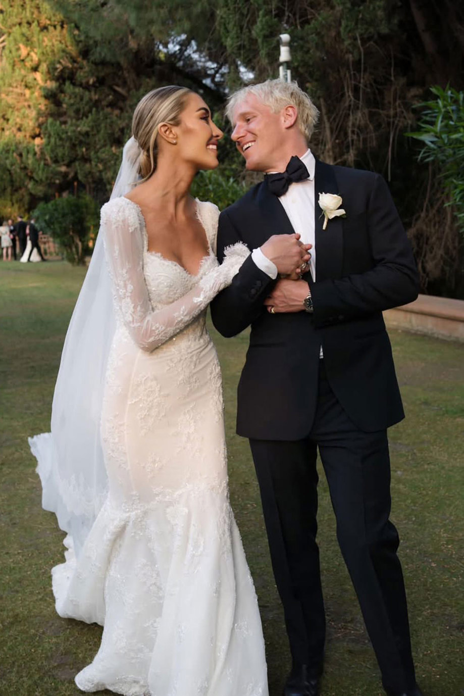 bride in long sleeve wedding dress and groom in black tux hold on to each other arm and smile face to face
