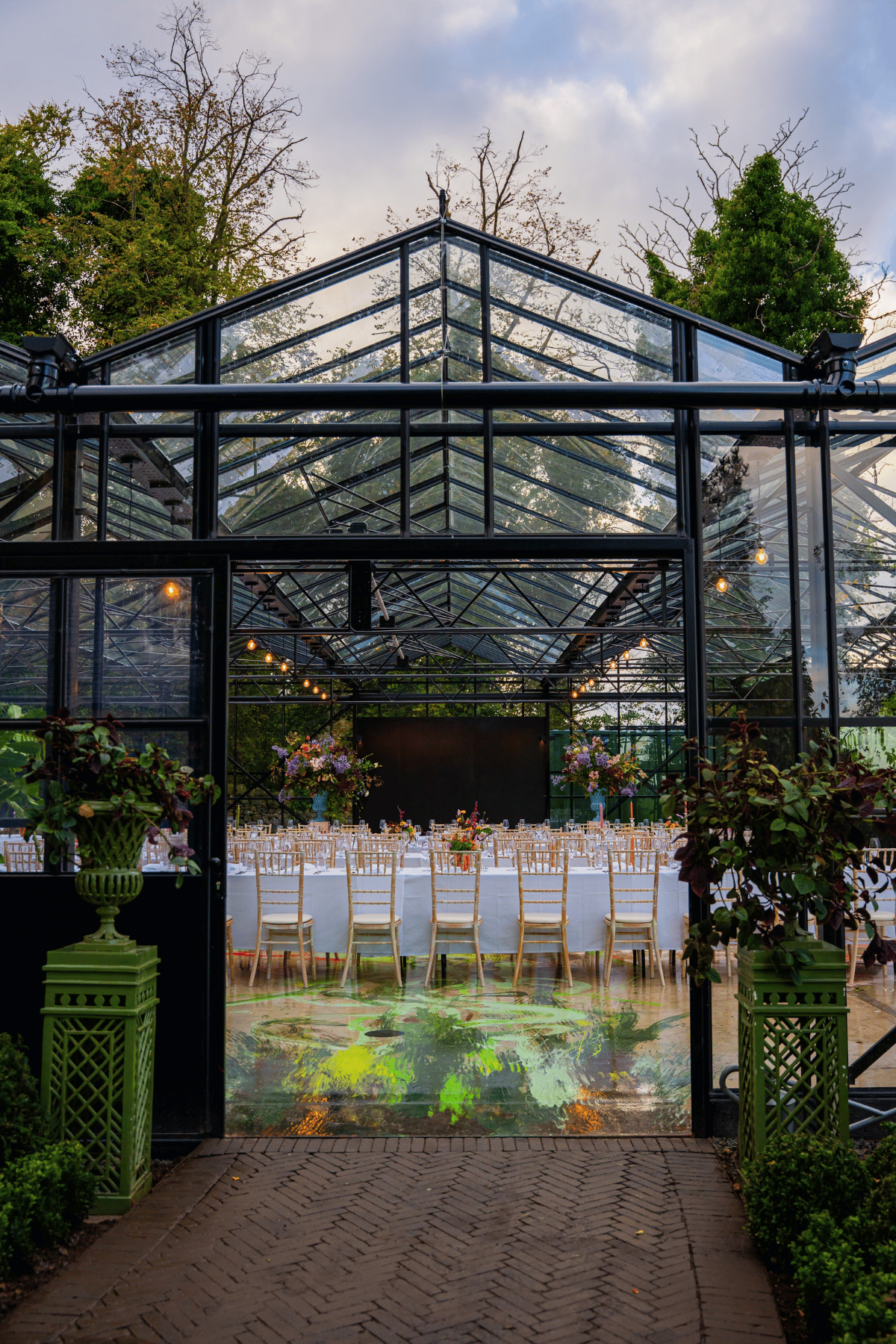 The Glasshouse at Jupiter Artland set for a wedding reception with long tables, flowers and transparent glass walls