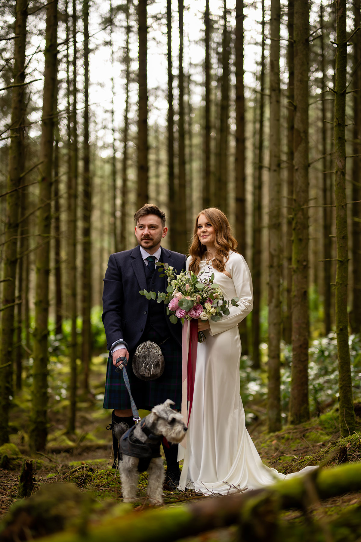 Bride and groom standing with their schnauzer dog in a woodland setting during their Glencoe elopement photoshoot