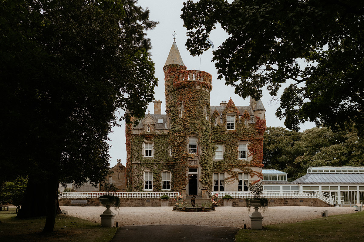 Exterior of Carlowrie Castle in Edinburgh, showcasing the ivy-covered stone façade, turreted architecture and glass Orangery surrounded by mature trees