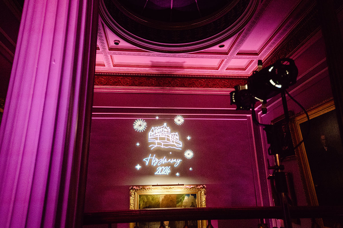 Pink uplighting inside the Signet Library with a custom wedding projection reading “Hogmanay 2024” alongside an illustration of Edinburgh Castle and fireworks