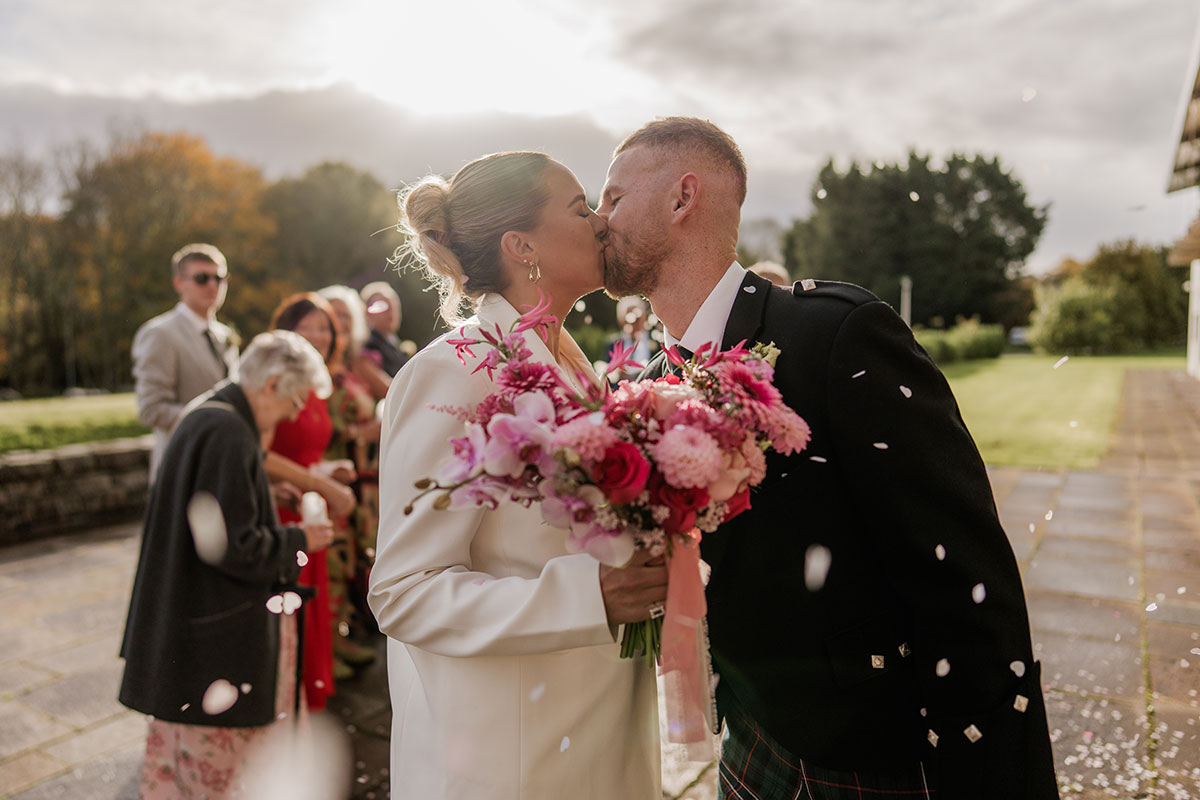 Bride and groom kiss during outdoor confetti moment after Scottish wedding ceremony