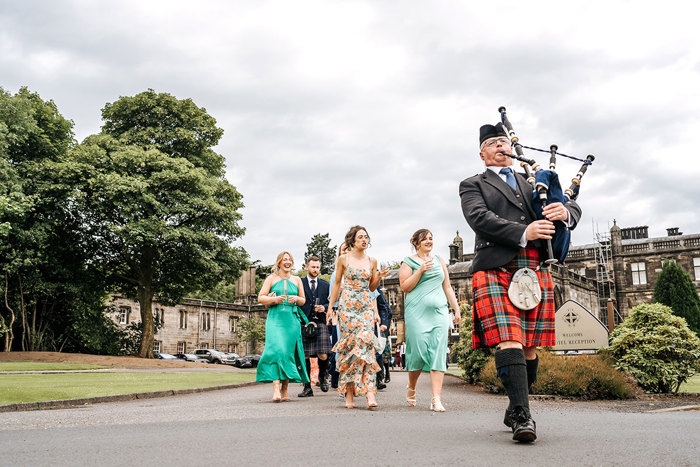 piper wearing a red kilt and carrying bagpipes lead guests at mar hall