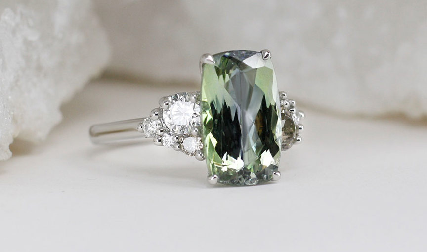a close up of a ring with large smoky green stone and diamond shoulders