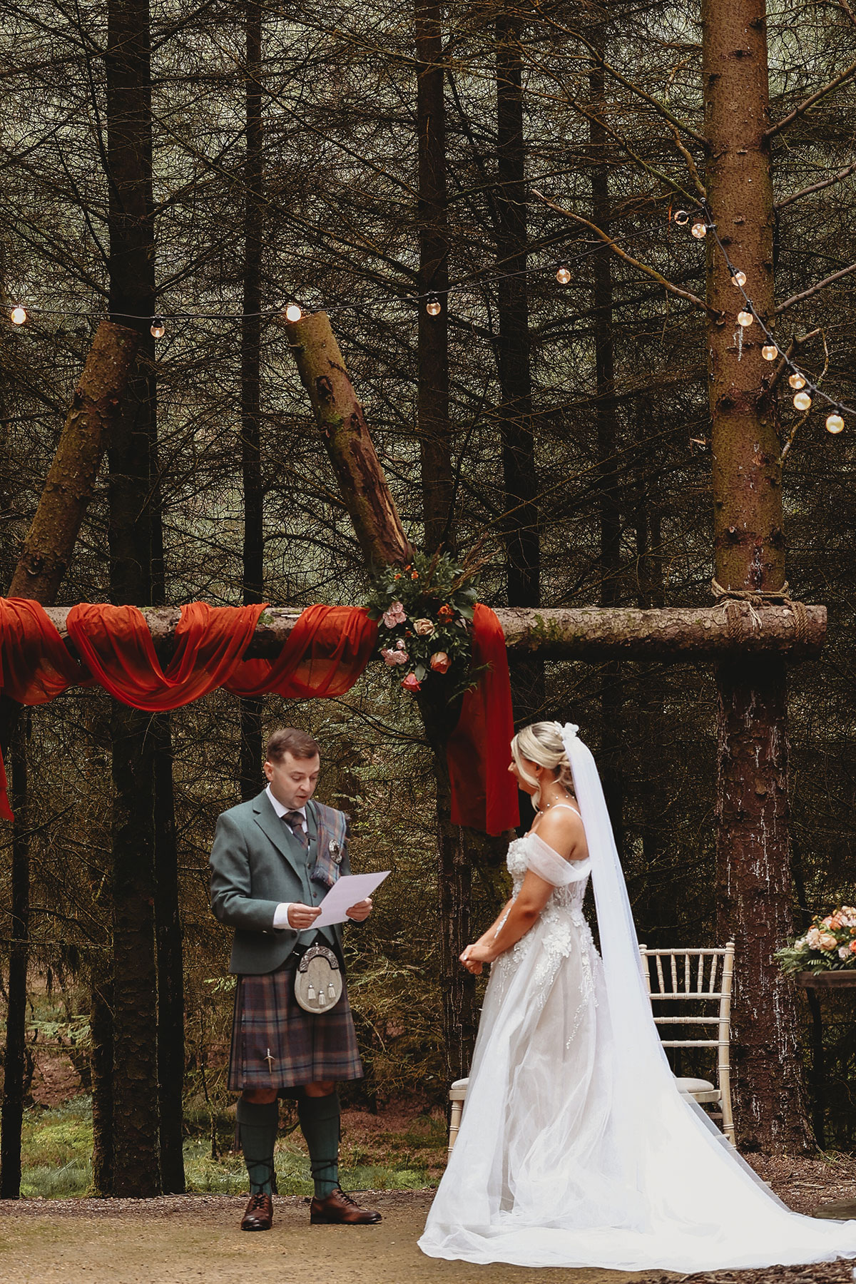 Bride and groom exchanging vows beneath a rustic wooden ceremony arch in a Scottish woodland wedding setting