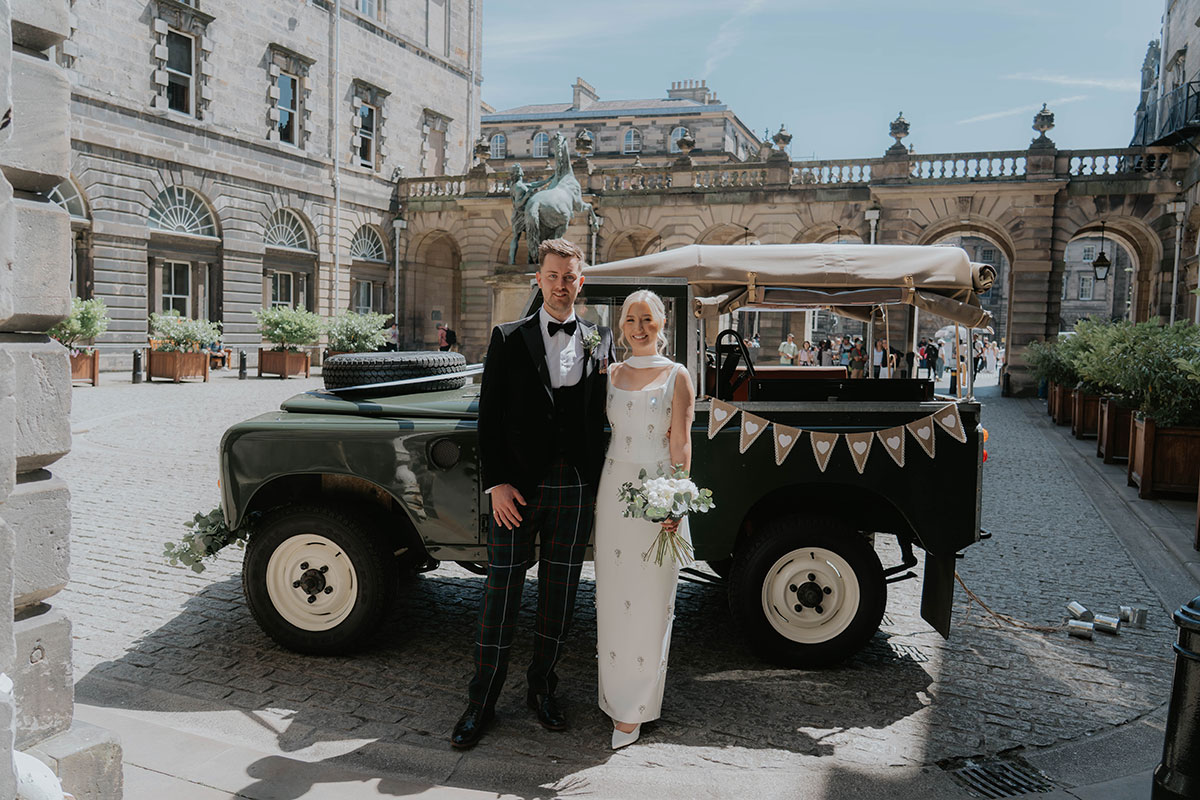 Newlyweds posing beside a vintage Land Rover in Edinburgh following their City Chambers wedding