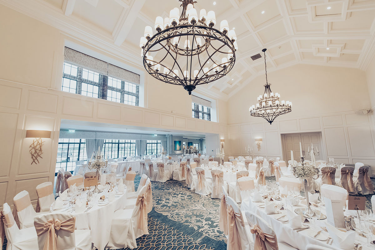 Wedding reception room at Western House Hotel arranged for dinner, with round tables, chandeliers and gold chair sashes.