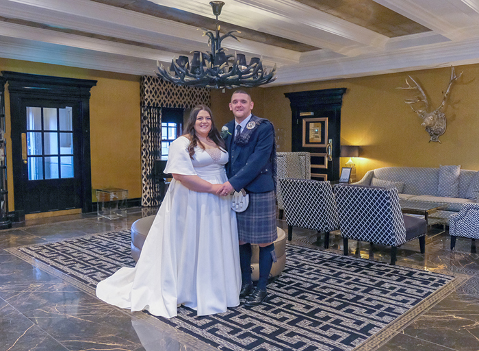 A bride and groom stand with their arms around each other in a room with a geometric rug and yellow walls