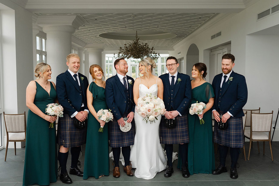 a group of people in wedding attire posing for a photo in the Conservatory at the Old Course Hotel.