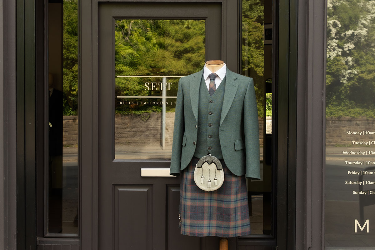 green jacket and corresponding tartan kilt on mannequin outside black door with SETT written across the glass, followed by kilts | tailoring