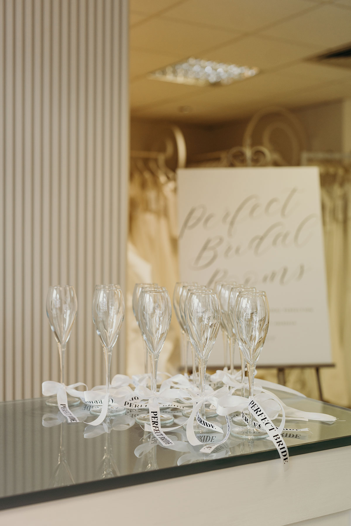 a collection of champagne glasses with 'perfect bride' ribbons tied around the stems