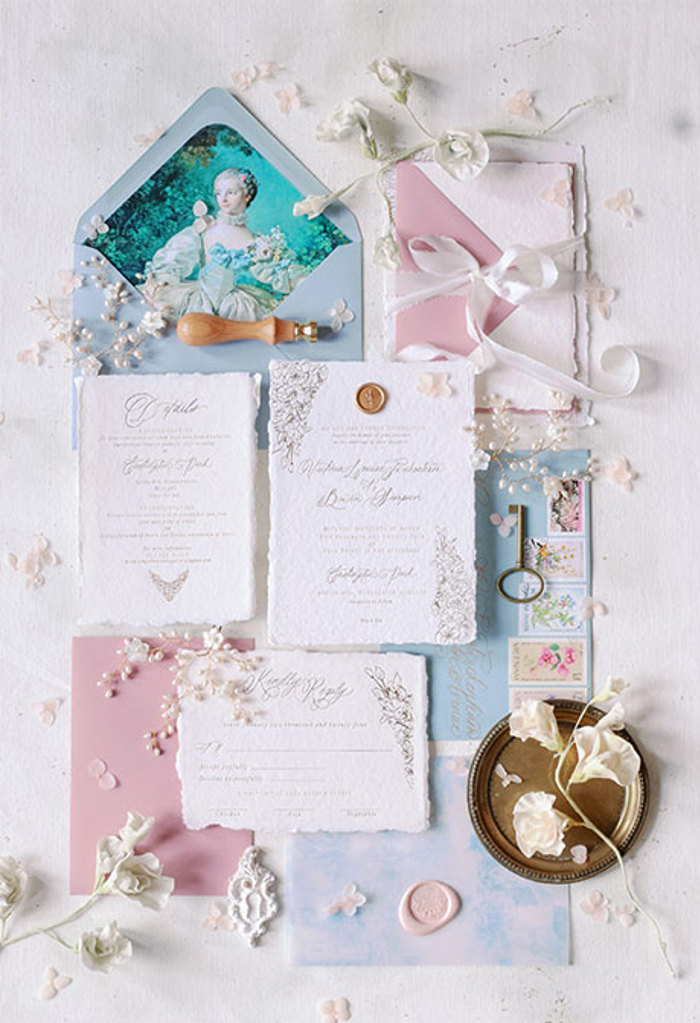 Pieces of card with cursive writing laid out with pastel coloured enveloped and gold wax seals