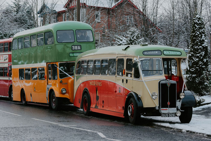 three vintage busses with white ribbons tied to their fronts parked on a street in the snow