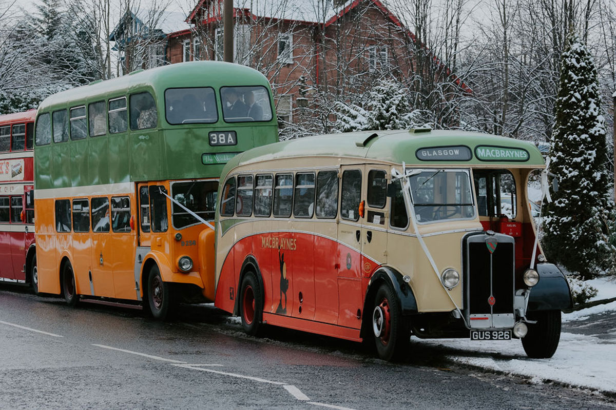 three vintage busses with white ribbons tied to their fronts parked on a street in the snow